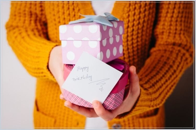 happy birthdayと書かれたメッセージカードと2つの小さなギフトボックスを手にもっている女性