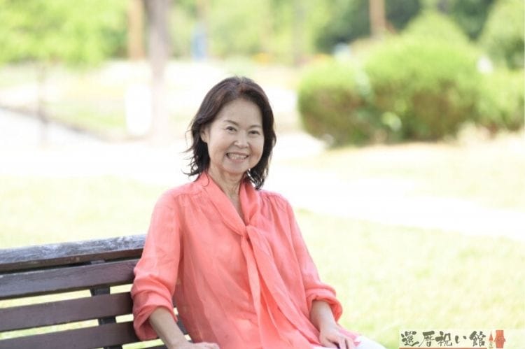 公園の椅子に座り微笑むシニア女性