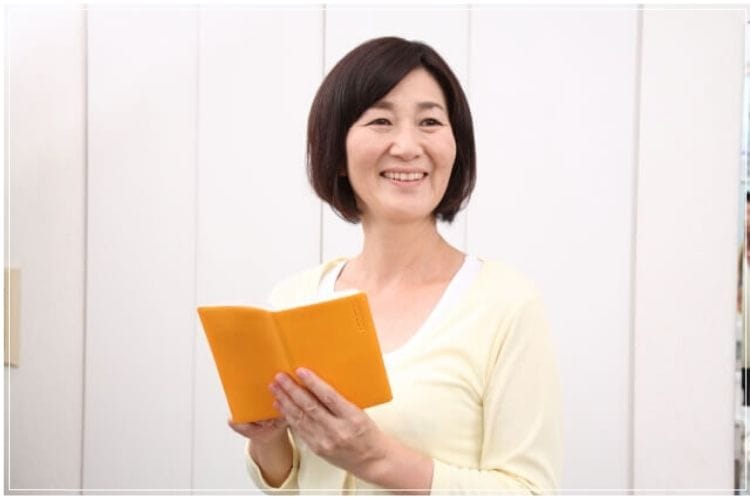 オレンジ色の手帳を持って微笑むシニア女性