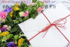 白の包みに赤く細い紐で四隅が結ばれた贈り物とピンクや青の造花の花