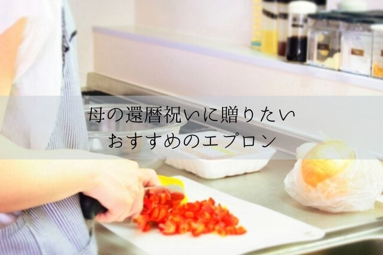 青のストライプのエプロンをつけた女性がまな板の上で赤と黄色のパプリカを細かく切っている