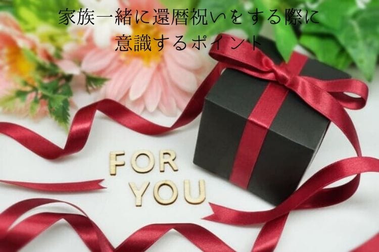 黒い包みにワインレッドのリボンがついたプレゼントボックスとピンクの花、そしてfor youと書かれた文字