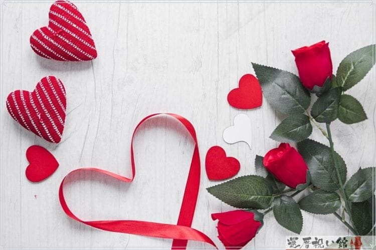 赤い薔薇とハート型の布の小物とハートをかたどるように置かれた赤いリボン