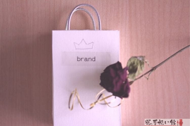 brandと書かれた白い紙袋にワインレッドの薔薇が1輪置かれている