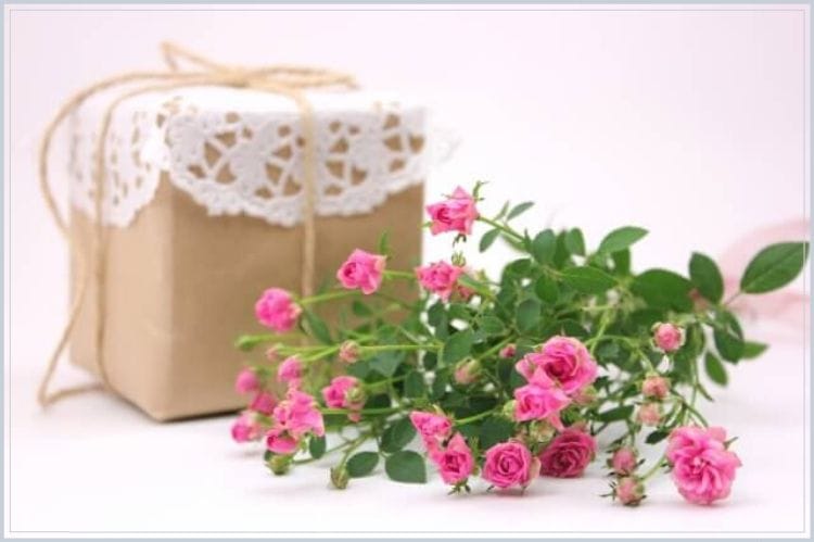 茶色の包みに包まれレースがかけられたギフトボックスとピンクの薔薇の花束