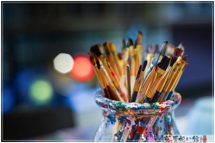 絵の具が飛び散ったガラスの瓶に絵の具筆がたくさん入っている