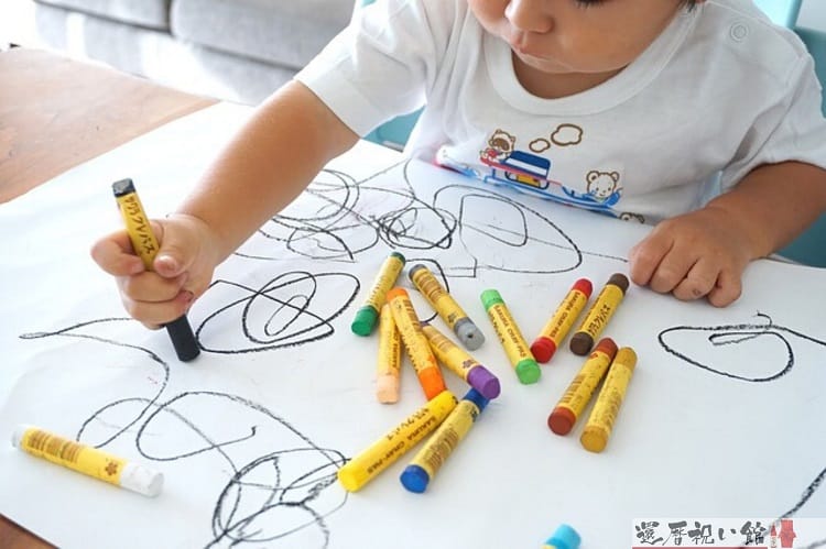 白い紙にクレヨンでお絵描きする子ども