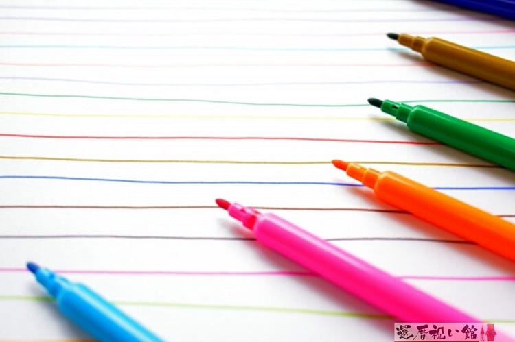 水色、ピンク、オレンジ、緑、茶色などの水性ペンとそのペンを使って白い紙に線を描いた様子