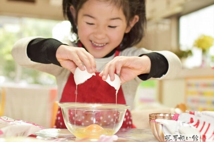女の子がボールに卵を割って料理を作っている様子