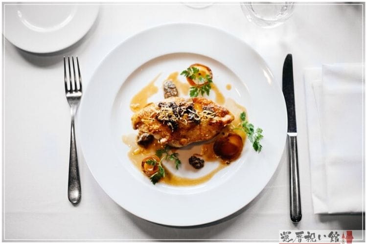 白い皿にソースがかけられた焼いた鶏肉が置かれている