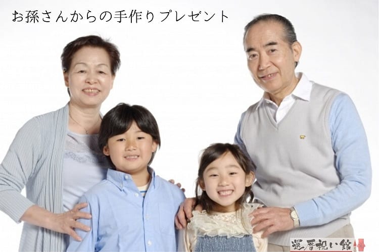 祖父母が孫の肩に手を置き4人で笑顔を作っている様子