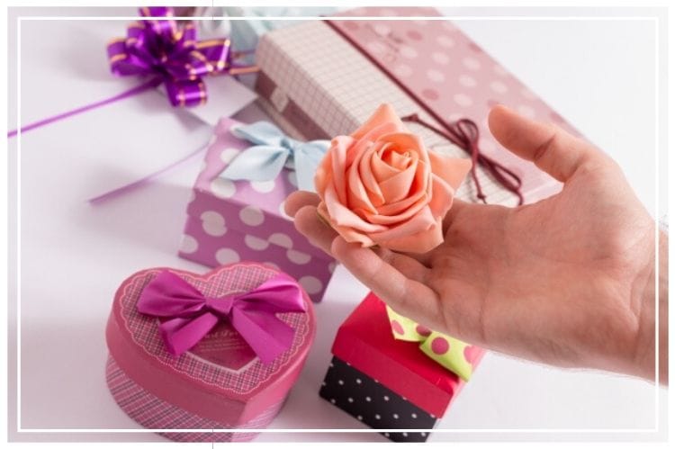 テーブルに様々な色・柄のプレゼントボックスが置かれていて、その上に薄いピンクの薔薇を持った手がある