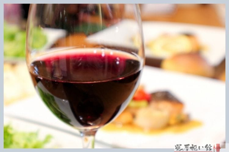 洋食のディナーが並ぶテーブルに置かれた赤ワインの入ったグラス