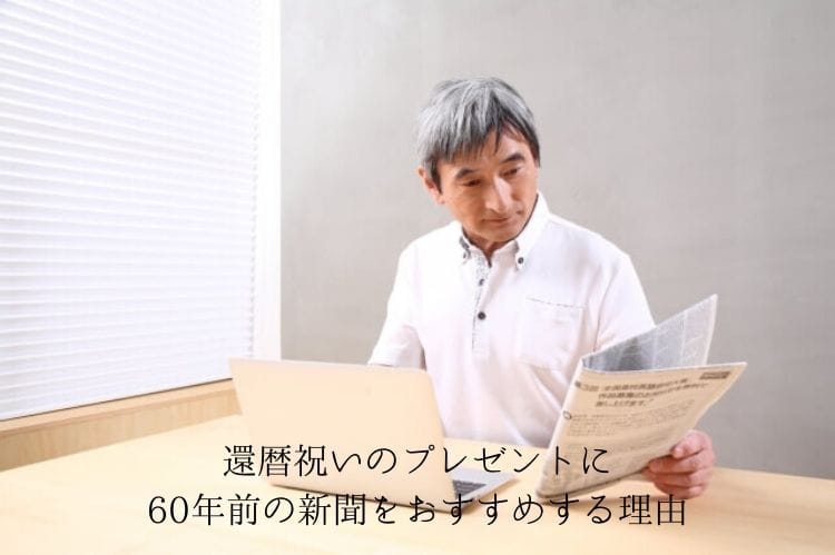 ノートパソコンを前に置きつつ新聞を読むシニア男性
