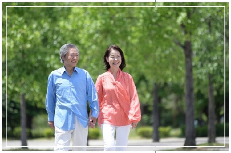 シニア夫婦が木が生い茂る場所を散歩している