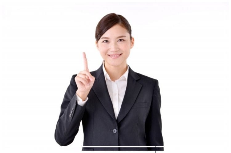 スーツを着た若い女性が指を立ててポイントを示している様子