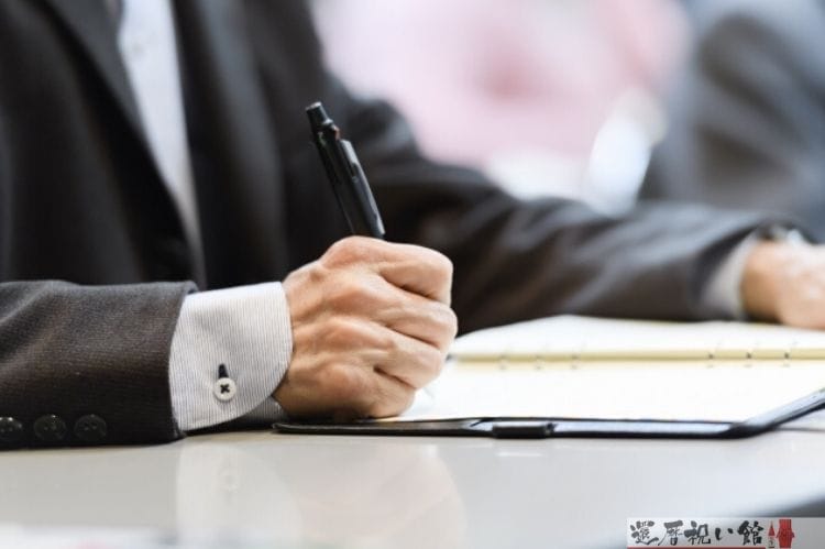 スーツを着た男性がボールペンを持ち何かを手帳に書いている