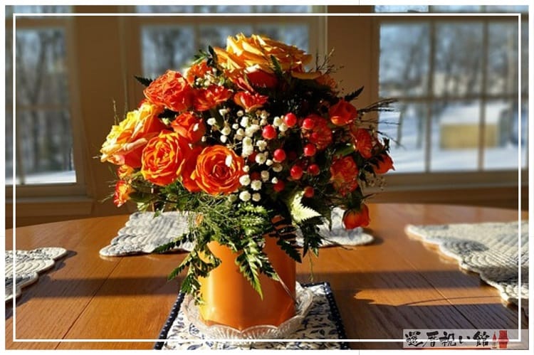 オレンジの花瓶にオレンジや黄色の薔薇が飾られている