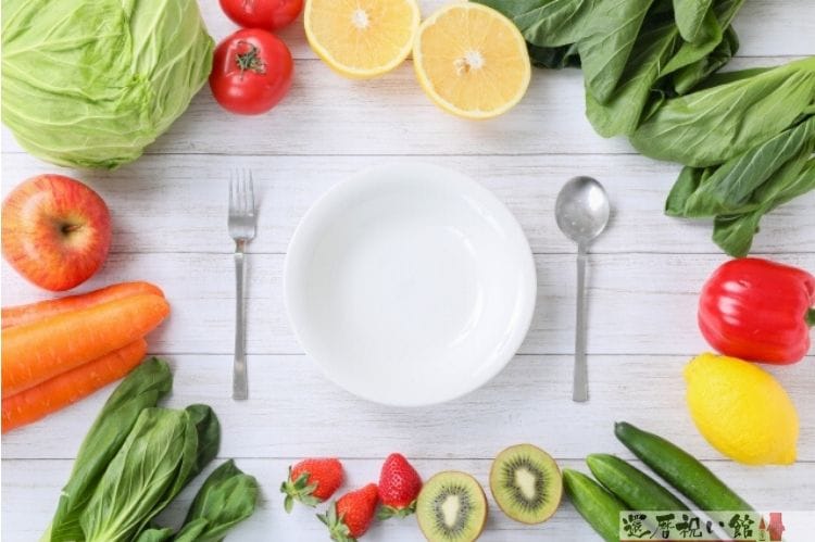 白い皿とその両脇にフォーク&ナイフ、その周りに野菜&フルーツが置いてある