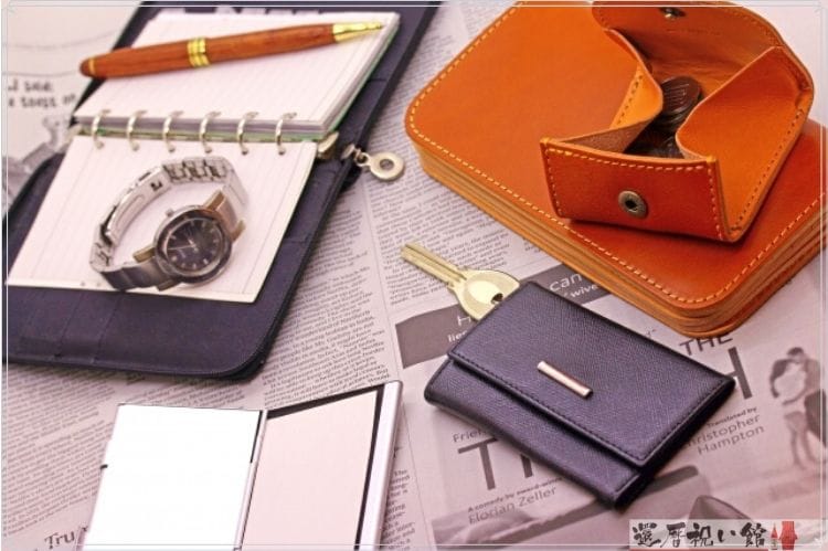 茶色の財布と黒のキーケースと腕時計や手帳、ボールペン