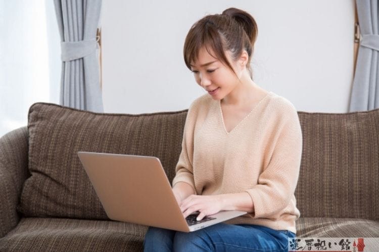 ソファに座りノートパソコンのキーボードを打っている女性