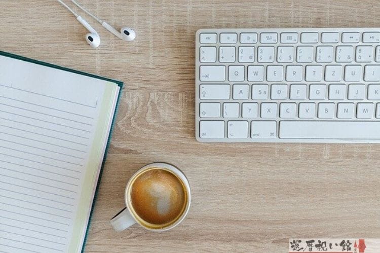 パソコンのキーボードとイヤホン、ノート、コーヒーが入ったマグカップ
