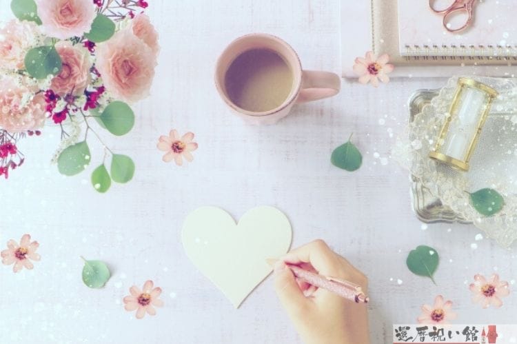 うすい黄色のハート型をしたメッセージカードにボールペンで何かを書こうとする女性の手