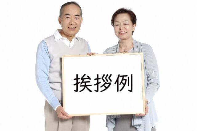 シニア夫婦が挨拶例と書かれた板を持っている