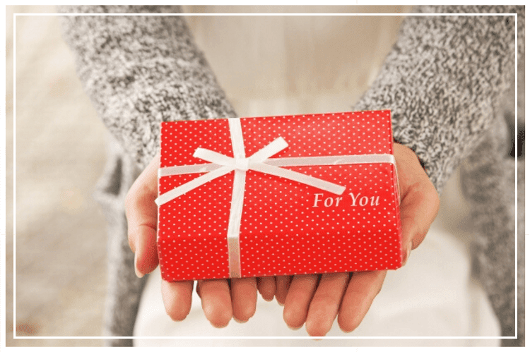 両手を合わせてその上に赤いプレゼントボックスを乗せている女性