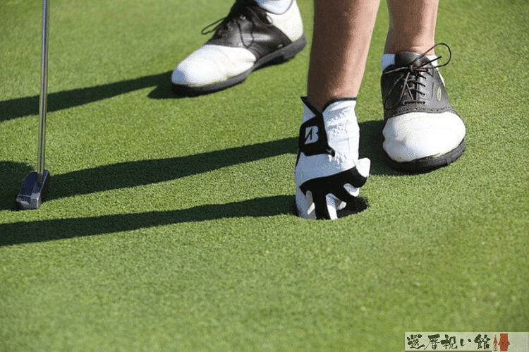 ゴルフ場でカップに入ったボールを取ろうとしている男性の足もと