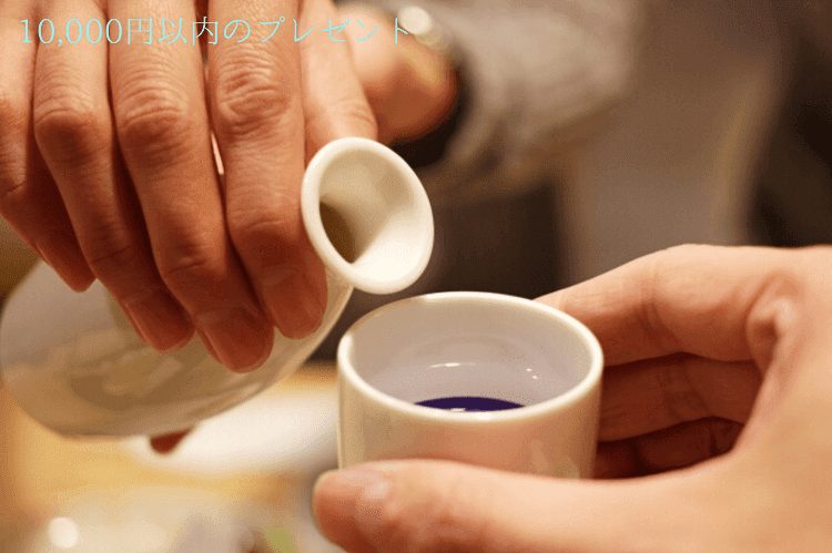 白い徳利から白いおちょこへ日本酒を注いでいる様子