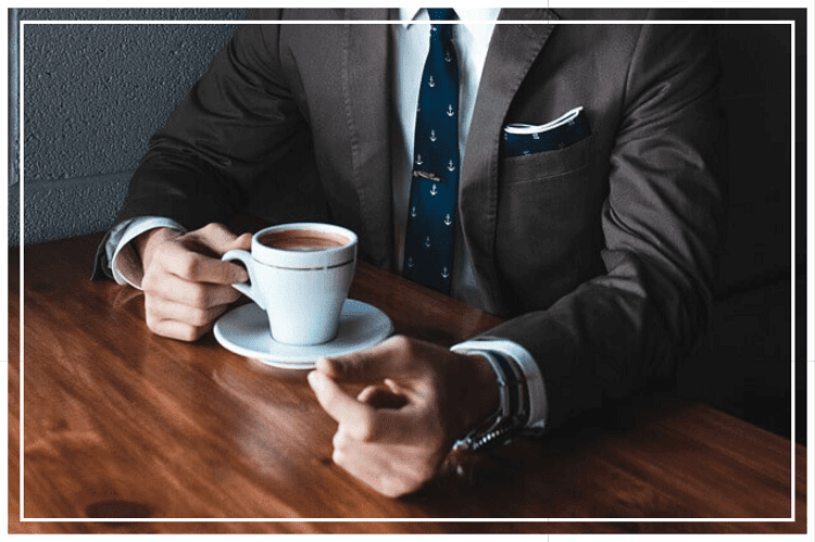 テーブルに座りコーヒーを飲もうとしているスーツを着た男性