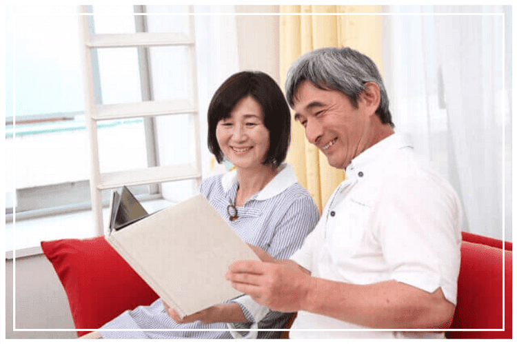ソファに座りアルバムを笑顔で眺めるシニア夫婦