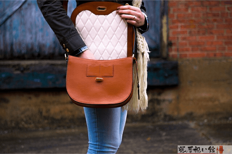 ブラウンの丸形ショルダーバッグを開けて中から何か取ろうとしている女性