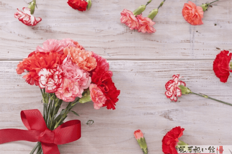 赤いリボンがついたカーネーションの花束とその周りにもちらばっておかれているカーネーション