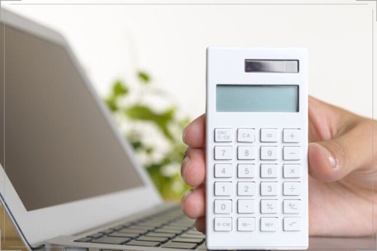 ノートパソコンの前で白い電卓を立てて持っている手