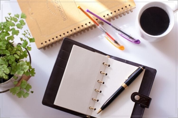 手帳、ボールペン、ノート、コーヒーが机に置いてある様子