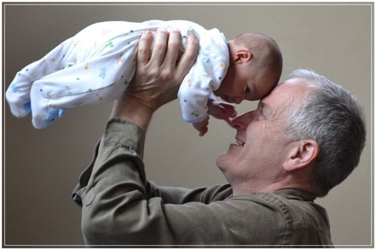 シニア男性が生まれたての赤ちゃんを抱っこして高く持ち上げている様子