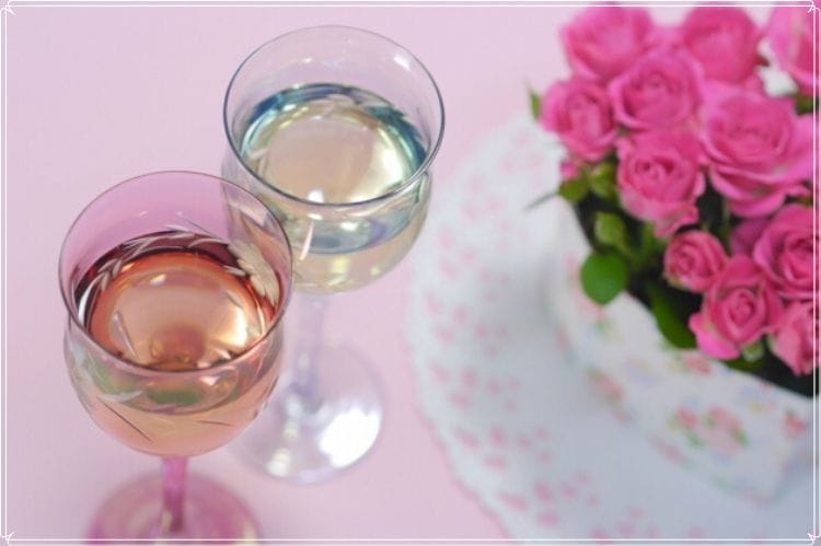 ピンクのバラの花束と白ワインもしくはシャンパンが入った2つのグラス