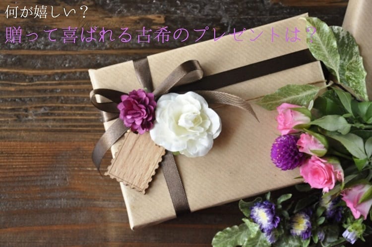 Un paquet brun avec un ruban brun foncé, des fleurs violettes, une carte de message et un bouquet de fleurs roses et violettes à côté.