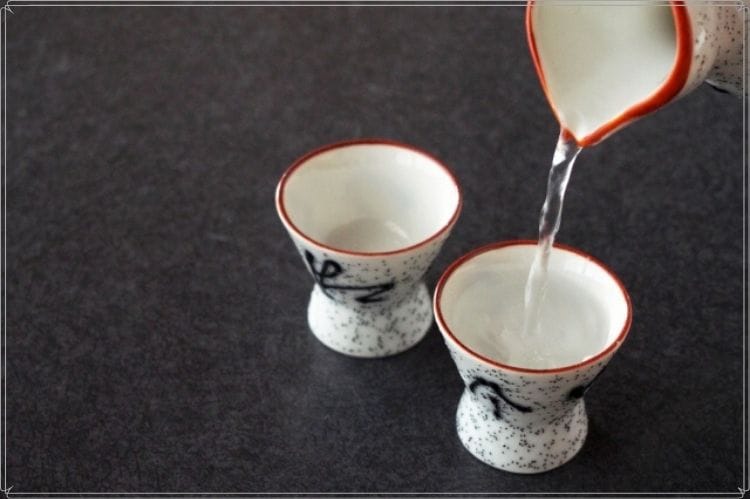 徳利に入った日本酒を2個のおちょこに入れている様子