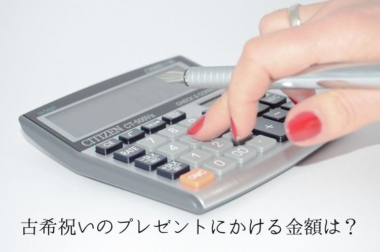 赤いマニキュアをした女性が灰色の電卓をペンを持ちながらたたいている