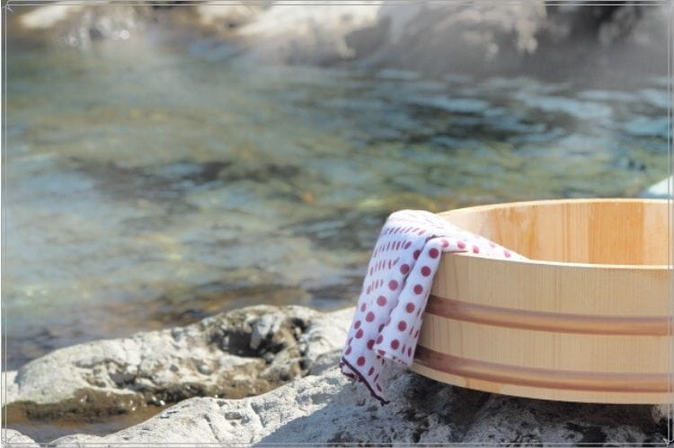 温泉の湯の脇に置いてある赤い水玉のてぬぐいが掛けてある木製の風呂桶