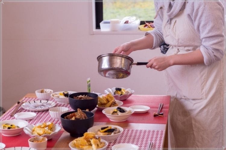 エプロンをつけた女性がテーブルに食事の準備をしている