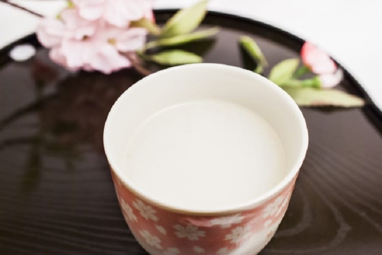 Amazake e uma flor rosa ao lado em uma xícara de chá de cor rosa