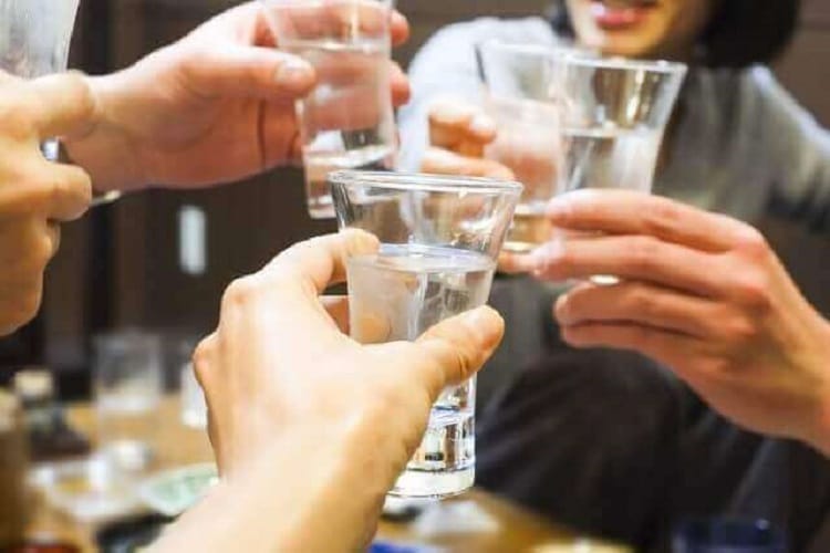 飲み会で日本酒が入ったグラスで乾杯する人たち