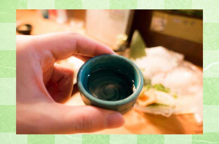 緑色のおちょこに日本酒が入っていて、それを手に掴んでいる様子