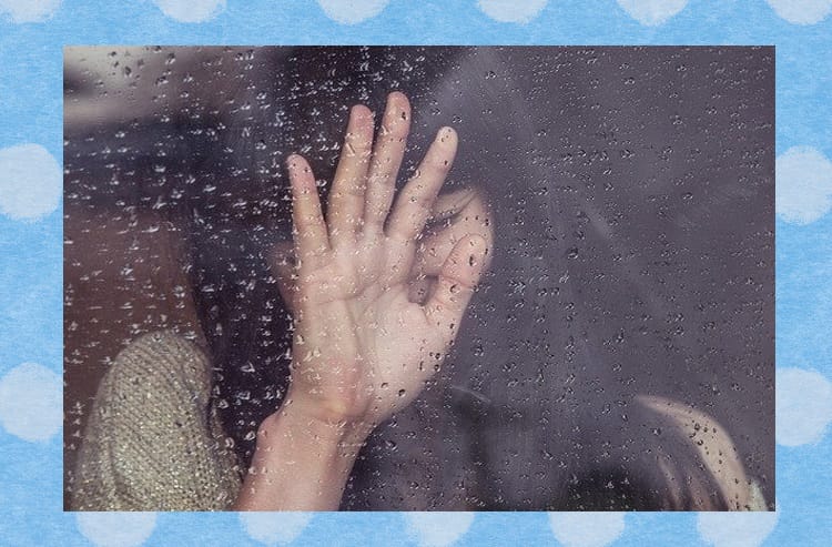 女性が家の中から雨でぬれた窓に手を触れて笑う様子